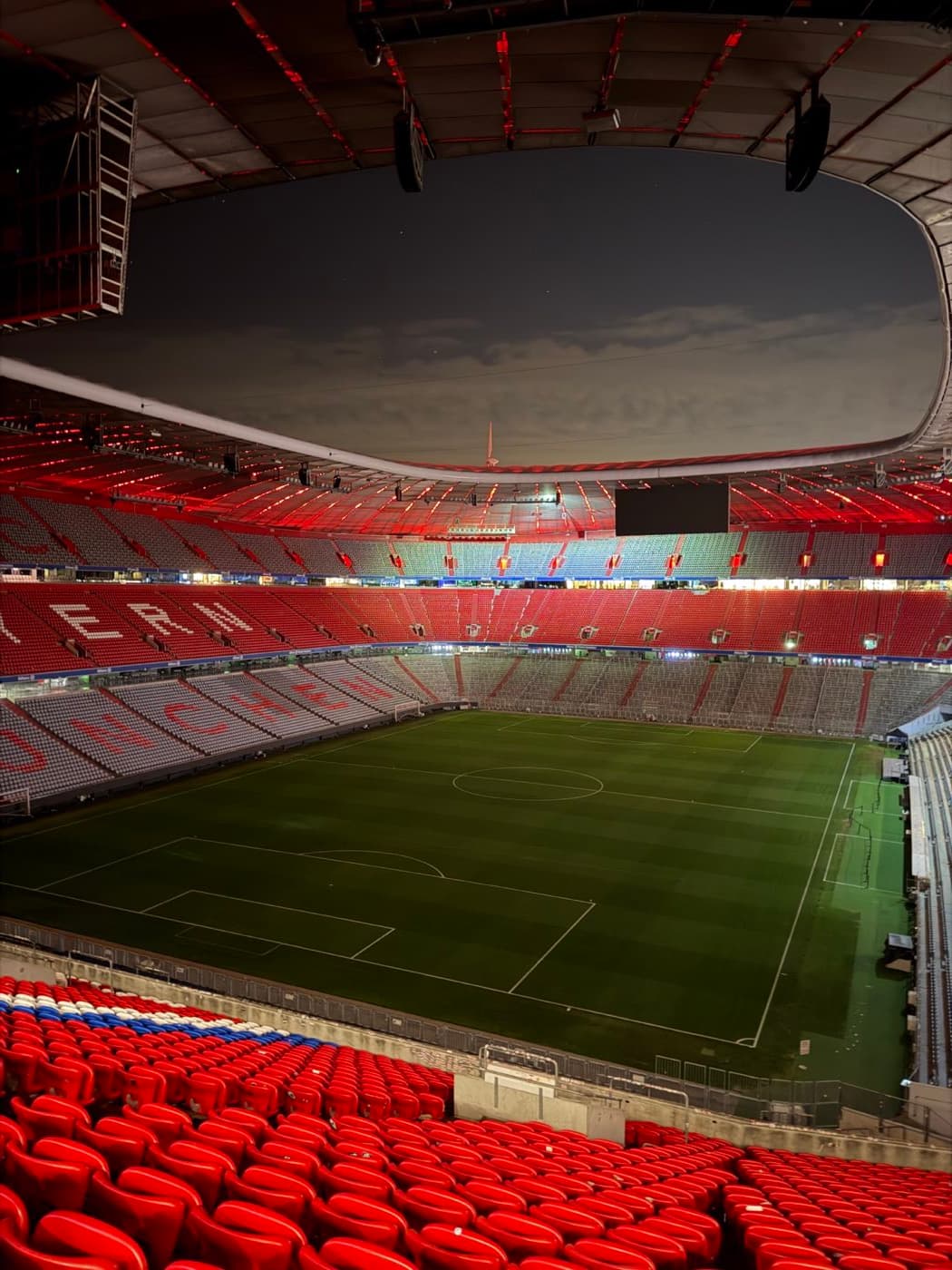 Abendlicher Innenblick in die beleuchtete Allianz Arena mit roten Sitzreihen und Spielfeld