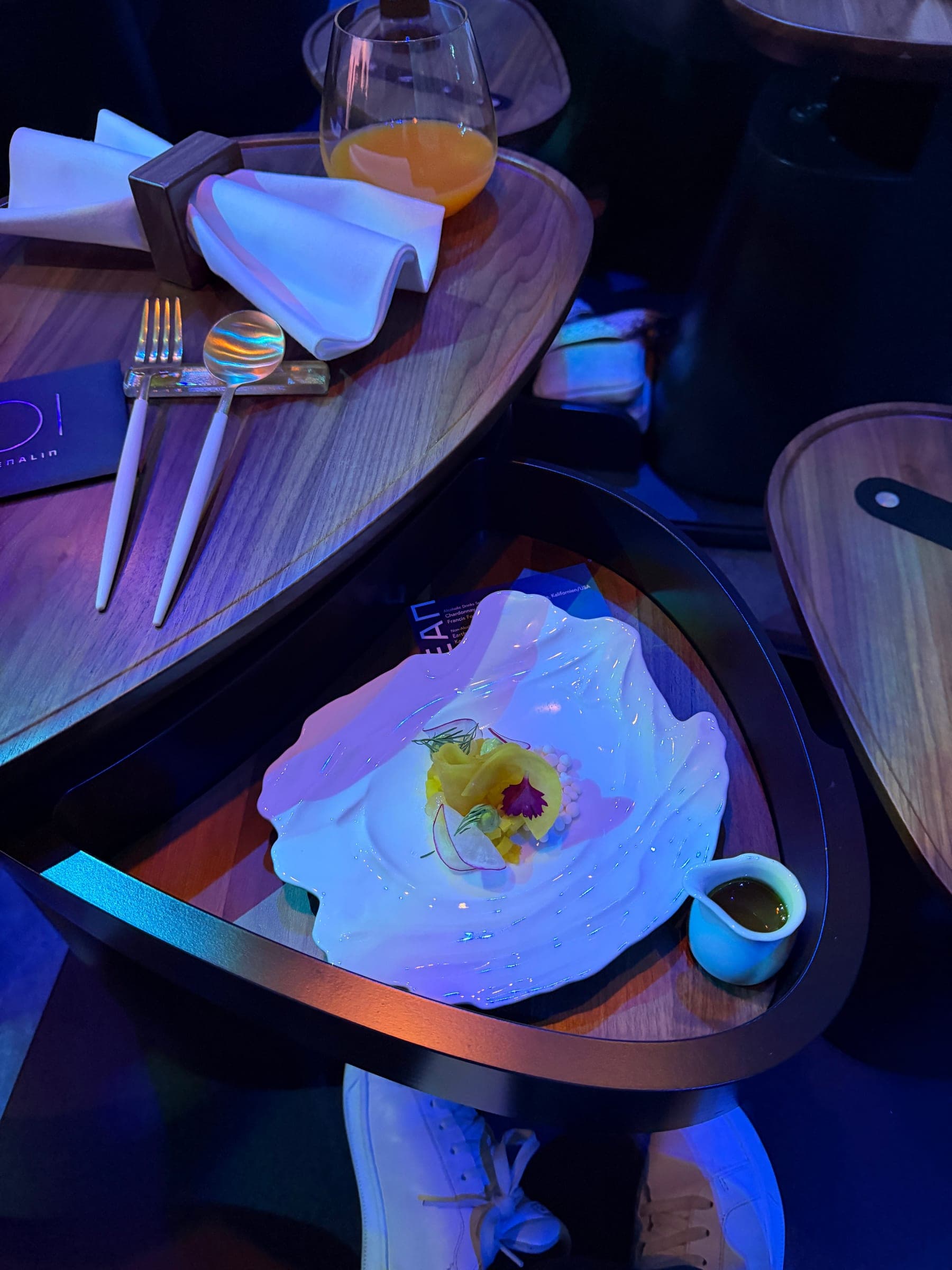 Tischdetail bei Eatrenalin mit Besteck, Getränk, blauer Lichtstimmung und angerichtetem Gang